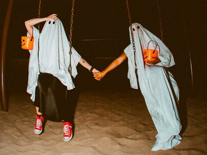 People in ghost costume at a Halloween, on swings.