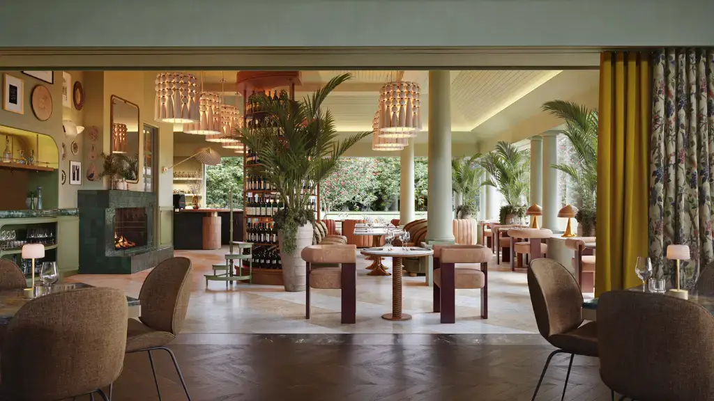 Stylish restaurant interior featuring warm tones, modern chandeliers, plush brown chairs, and large potted plants. The atmosphere is inviting and elegant.