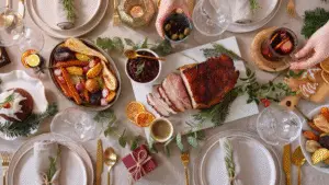Festive table setting with a glazed ham centerpiece, roasted vegetables, cranberries, and mulled wine. Elegant, warm, and inviting atmosphere.
